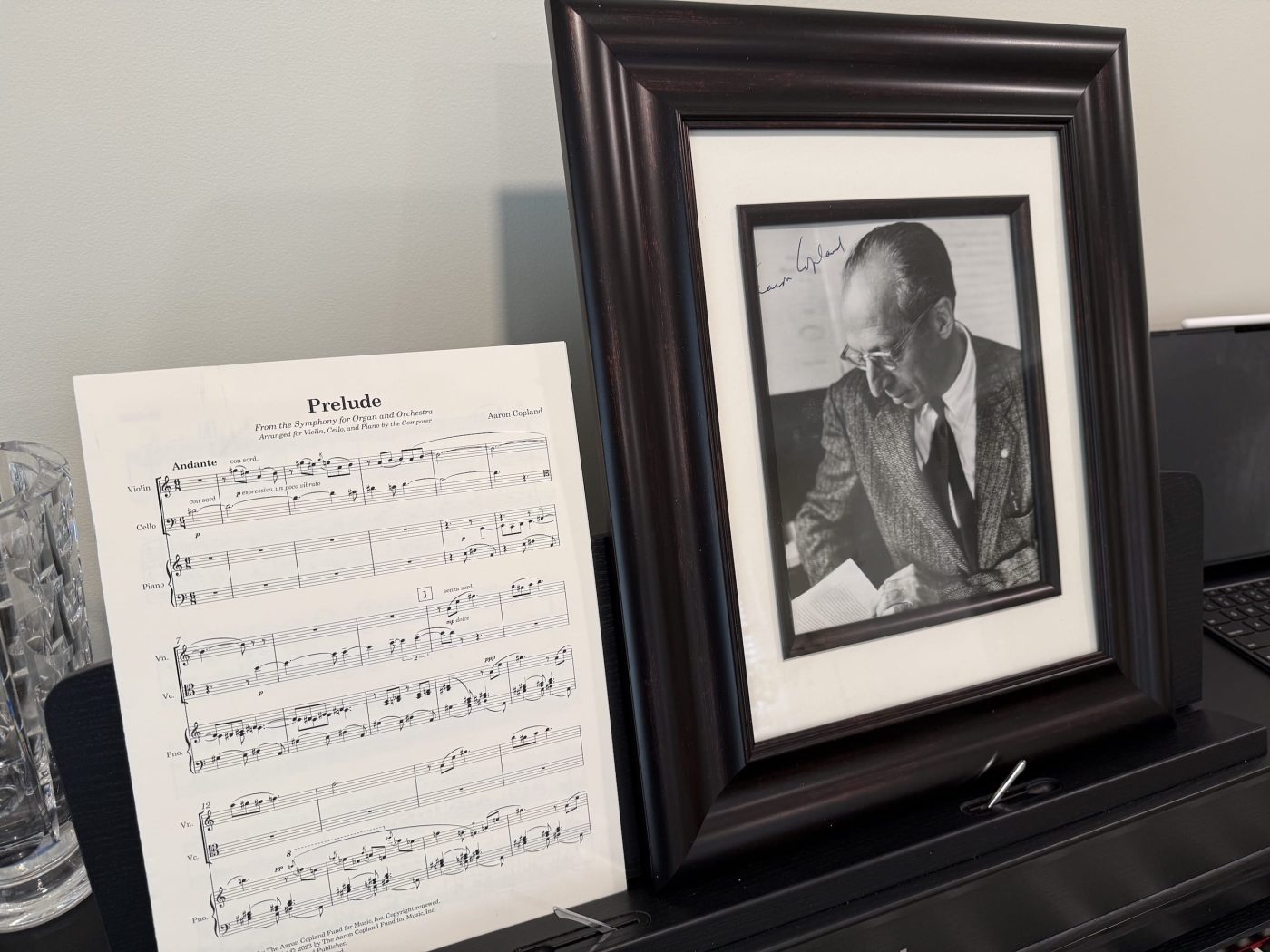 The opening page of Aaron Copland’s Prelude for violin, cello and piano beside a framed portrait of the composer.