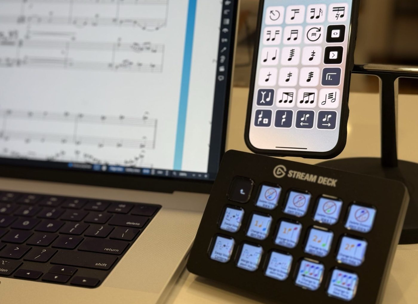 A laptop showing a score in a notation program, a phone displaying a keypad of notation commands, and an Elgato Stream Deck whose illuminated keys carry the same notation symbols.
