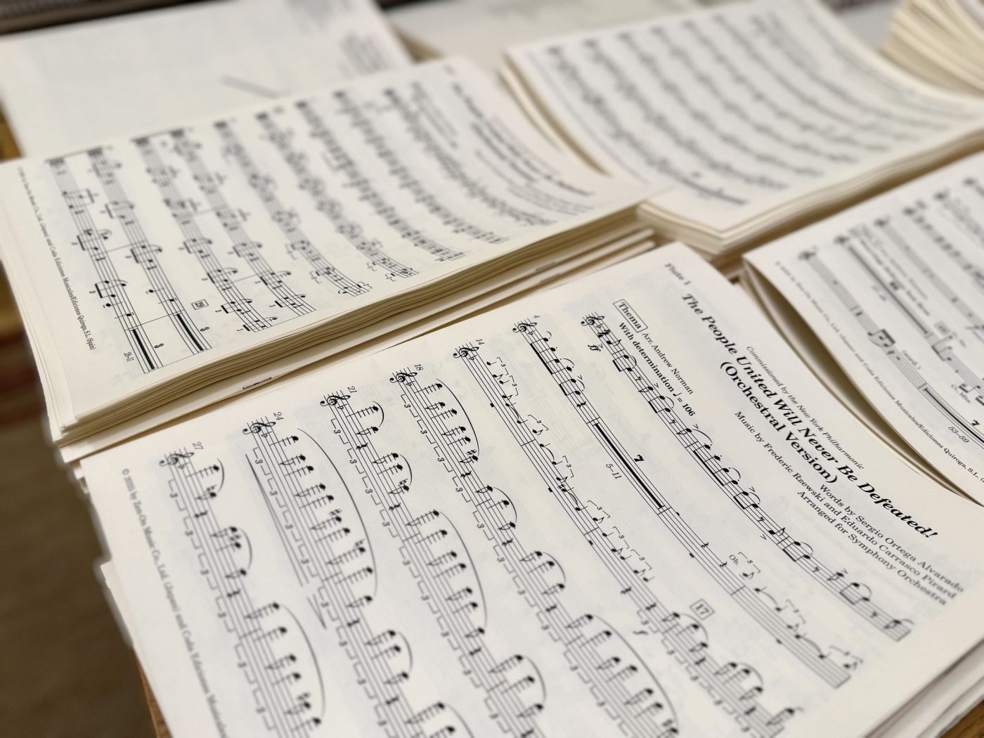 Freshly printed orchestral parts fanned across a table, the open part headed Flute 1, The People United Will Never Be Defeated! (Orchestral Version), commissioned by the New York Philharmonic, music by Frederic Rzewski.